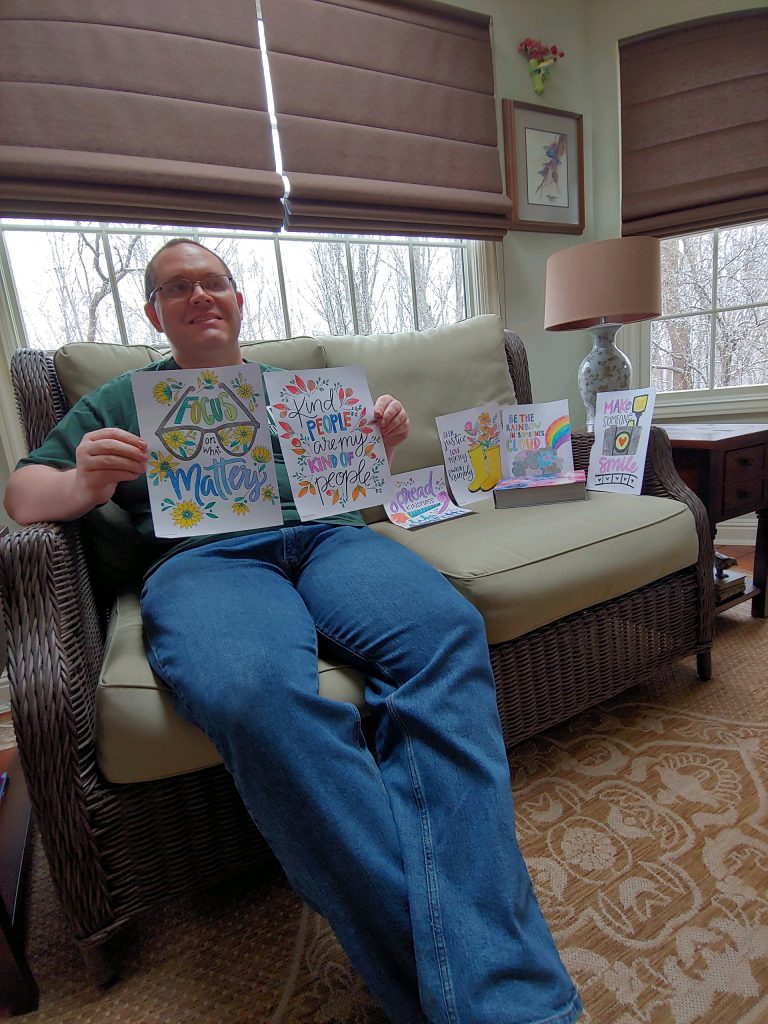 Club Create member showing all of his artwork sitting on his couch