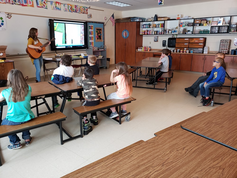 MiAA Teaching Artist Kerry Yost playing her guitar in front of a class of elementary students