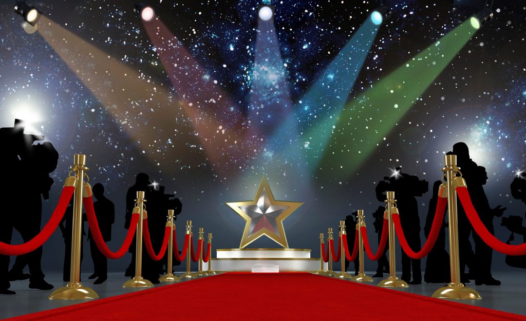 A red carpet leading to a platform with a giant gold star standing on it and lights beaming down on it - like Hollywood