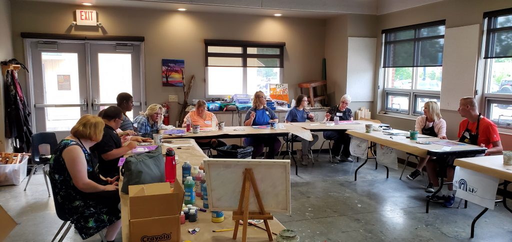 Club Create Members working working on their painting around long tables organized in a horseshoe shape