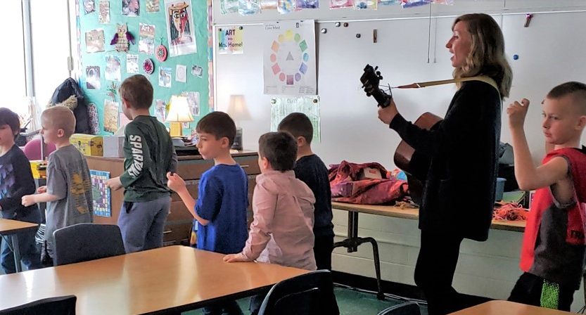 Kerry Yost plays guitar as she marches with young students around the classroom