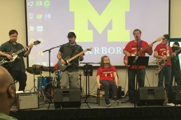 A rock band on stage featuring students with disabilities playing bass, guitar, drums, keyboard and singing