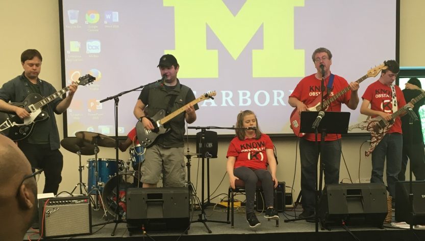 A rock band on stage featuring students with disabilities playing bass, guitar, drums, keyboard and singing