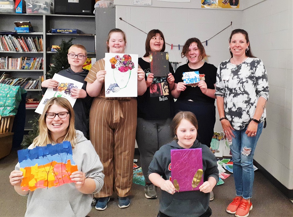Smiling students hold up their artwork with artist Mandy Loyselle