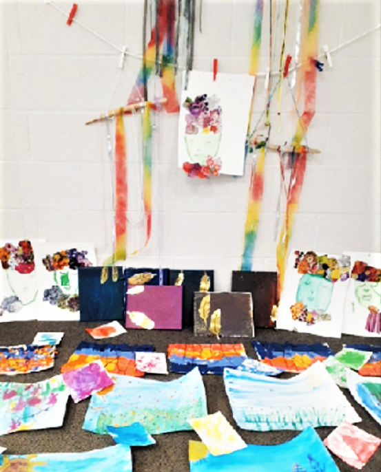 multiple dream catchers hanging on a wall, with student paintings, drawing and collages laying on the floor in a display of all the residency artwork