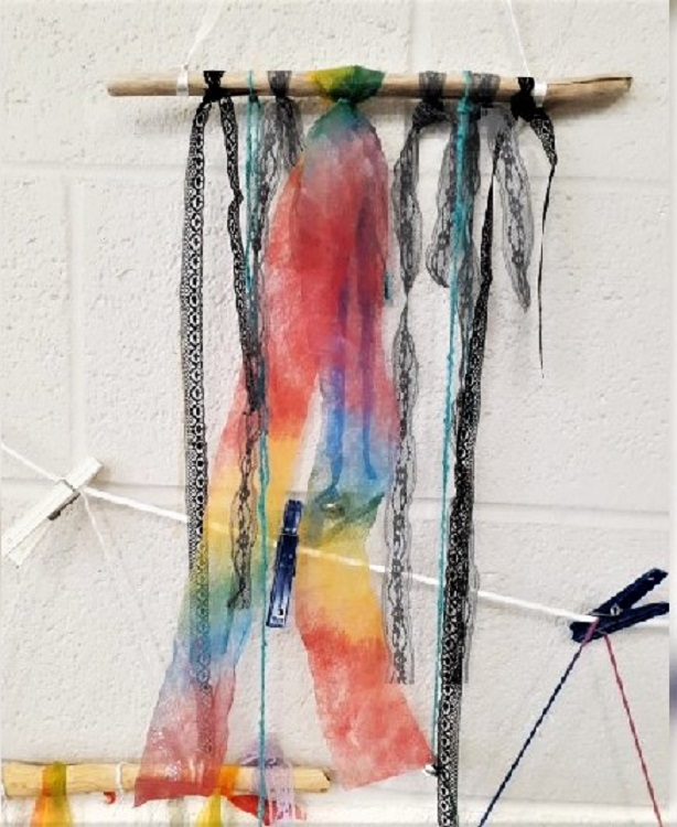 Dream catcher with a branch across the top holding wrapped in multi color sheer cloth.
