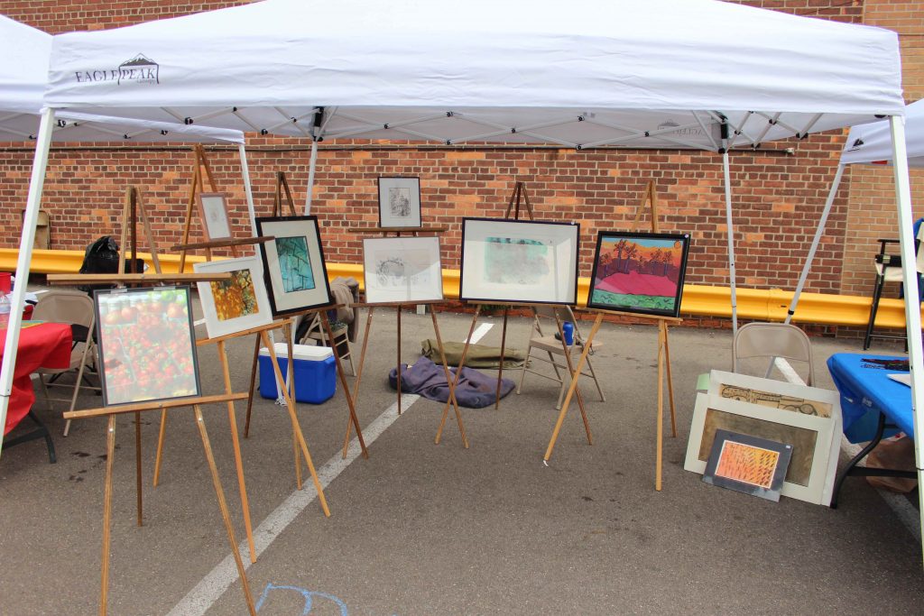 Framed artwork from MiAA artists with disabilities on easels in an art fair booth