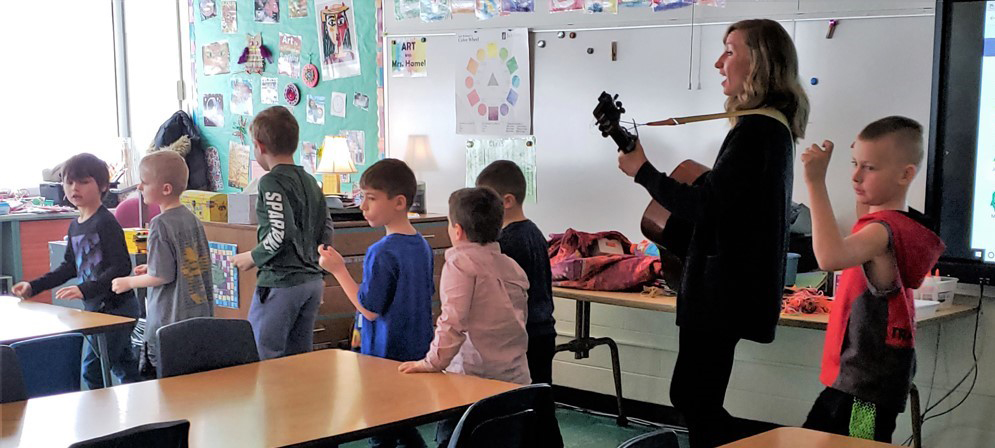 Guitarist Carrie Yost leading elementary students around a classroom as they sing