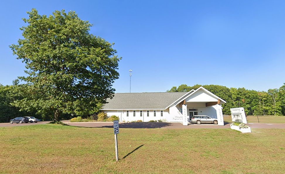 small white church with a gray roof surrounded by a large green field