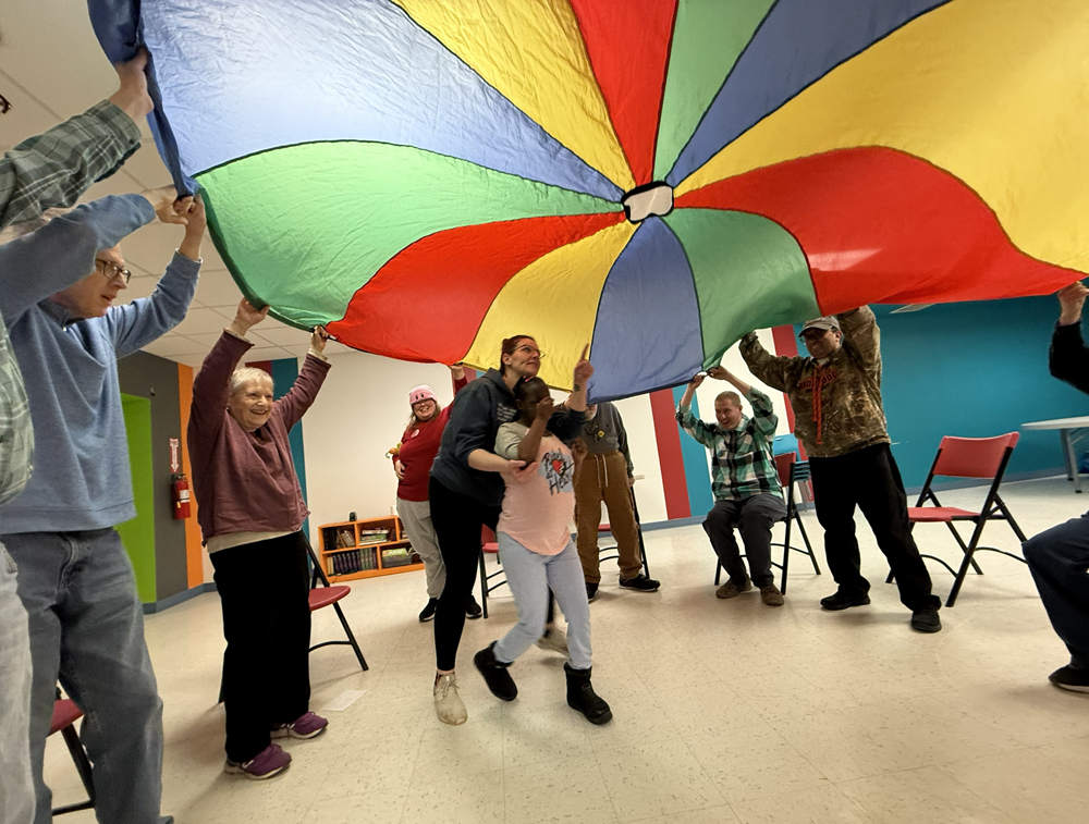 Club Create members lifting a multi colored parachute with a member improvising a dance under it